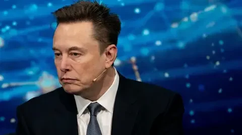 Getty Images Close up of Elon Musk wearing a suit against a blue background