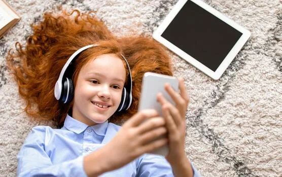 Digital Natives. Overhead Above Top High Angle View Of Cheerful Gen Z Girl Lying On The Floor Carpet In Bedroom, Listening To Music In Wireless Headset, Using Smartphone, Taking Selfie, Watching 68088924